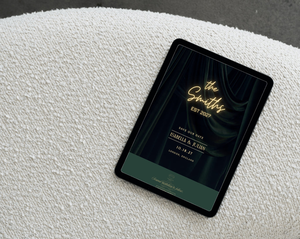 Art deco save the date website open on a tablet resting on cream boucle, showing the neon marquee with the couple's names, wedding date and city.