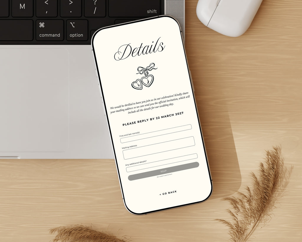 Art deco save the date details page on a phone beside a keyboard and pampas grass, showing the reply-by date and the guest address form.